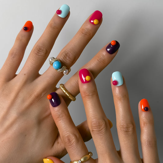 Close-up of hands with colorful nail art and rings on a neutral background