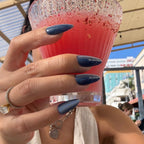 Hand holding a pink drink with a glittery rim, wearing a ring and bracelet, against an outdoor background.