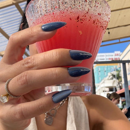 Hand holding a pink drink with a glittery rim, wearing a ring and bracelet, against an outdoor background.